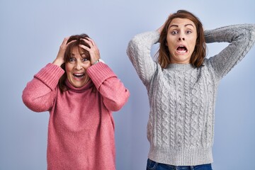 Sticker - Mother and daughter standing over blue background crazy and scared with hands on head, afraid and surprised of shock with open mouth