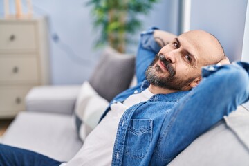 Poster - Young bald man relaxed with hands on head sitting on sofa at home