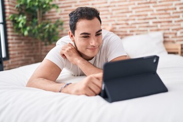 Sticker - Young hispanic man watching video on touchpad lying on bed at bedroom