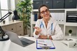 © Krakenimages.com - Young hispanic woman wearing doctor uniform and stethoscope smiling cheerful offering palm hand giving assistance and acceptance.