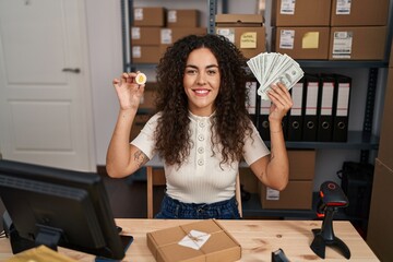 Poster - Young hispanic woman working at small business ecommerce holding money and bitcoin smiling with a happy and cool smile on face. showing teeth.