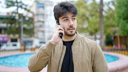 Wall Mural - Young hispanic man talking on smartphone with serious expression at park