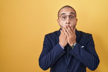 Poster - Hispanic man with beard wearing suit and tie shocked covering mouth with hands for mistake. secret concept.