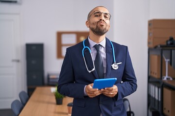 Canvas Print - Hispanic man with beard wearing doctor stethoscope working at the office looking at the camera blowing a kiss being lovely and sexy. love expression.