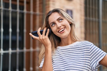 Canvas Print - Young blonde woman miling confident listening audio message by the smartphone at street