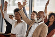 © Tshidzumba/peopleimages.com - Happy business people, workshop or hands up for participation in seminar for learning skills in office. Vote, men or women in audience together for group mentorship, training or coaching in workplace