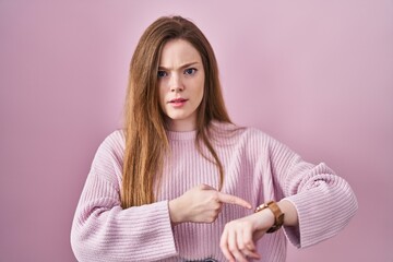 Sticker - Young caucasian woman standing over pink background in hurry pointing to watch time, impatience, upset and angry for deadline delay