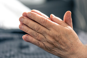 The hands of an elderly woman folded in prayer.