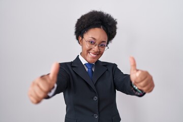 Poster - Beautiful african woman with curly hair wearing business jacket and glasses approving doing positive gesture with hand, thumbs up smiling and happy for success. winner gesture.