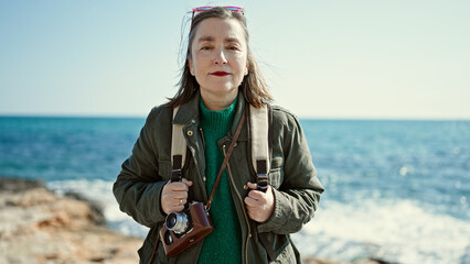 Sticker - Mature hispanic woman with grey hair tourist wearing backpack looking serious at the camera at seaside