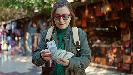 Sticker - Mature hispanic woman with grey hair tourist wearing backpack counting money at street market