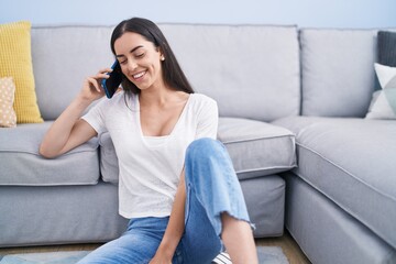 Wall Mural - Young hispanic woman talking on the smartphone sitting on floor at home