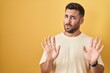© Krakenimages.com - Handsome hispanic man standing over yellow background moving away hands palms showing refusal and denial with afraid and disgusting expression. stop and forbidden.