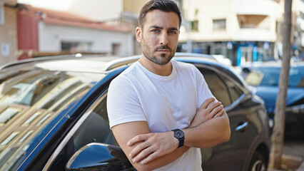 Poster - Young hispanic man standing with arms crossed gesture by car at street