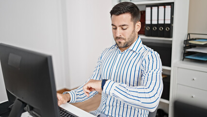 Poster - Young hispanic man business worker using computer looking watch at office