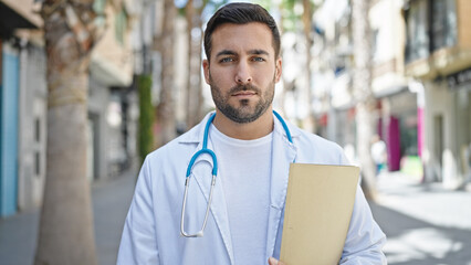 Poster - Young hispanic man doctor holding medical report standing with relaxed expression at street