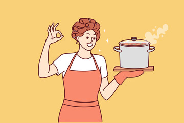 Woman housewife or cook with soup pan shows ok gesture and looks at screen smiling. Happy girl housewife in apron invites to have lunch and eat homemade food from healthy ingredients