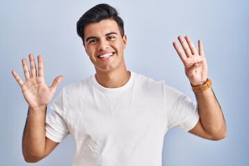 Poster - Hispanic man standing over blue background showing and pointing up with fingers number nine while smiling confident and happy.