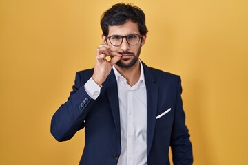 Canvas Print - Handsome latin man standing over yellow background mouth and lips shut as zip with fingers. secret and silent, taboo talking