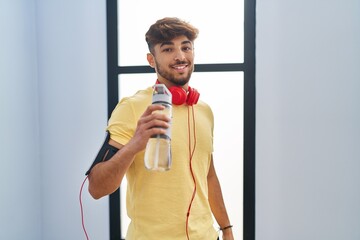 Sticker - Young arab man drinking water wearing headphones at sport center