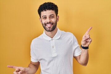 Sticker - Arab man standing over yellow background smiling confident pointing with fingers to different directions. copy space for advertisement