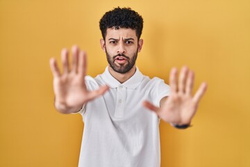 Sticker - Arab man standing over yellow background doing stop gesture with hands palms, angry and frustration expression