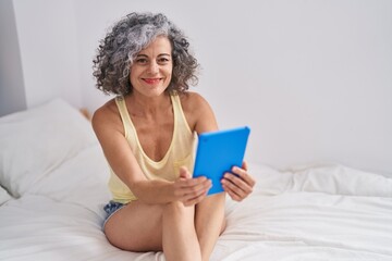 Wall Mural - Middle age grey-haired woman using touchpad sitting on bed at bedroom