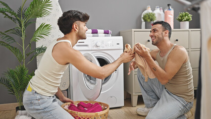 Wall Mural - Two men couple smiling confident washing clothes at laundry room