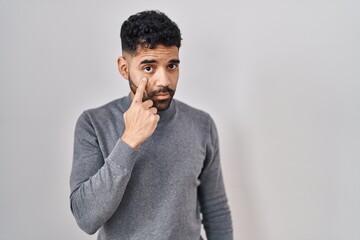 Poster - Hispanic man with beard standing over white background pointing to the eye watching you gesture, suspicious expression