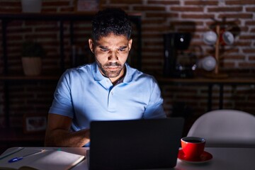 Wall Mural - Hispanic man with beard using laptop at night skeptic and nervous, frowning upset because of problem. negative person.