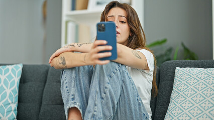 Wall Mural - Young beautiful hispanic woman sitting on the sofa using smartphone crying at home