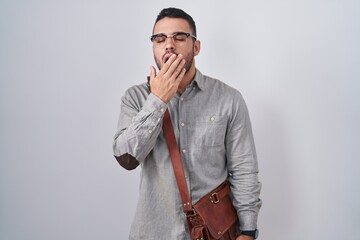 Wall Mural - Young hispanic man wearing suitcase bored yawning tired covering mouth with hand. restless and sleepiness.