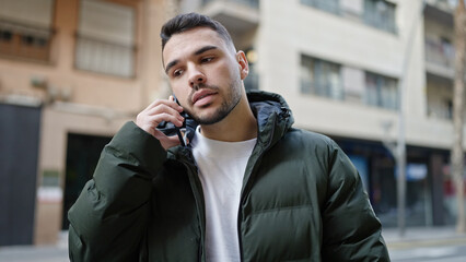 Wall Mural - Young hispanic man talking on smartphone with serious expression at street