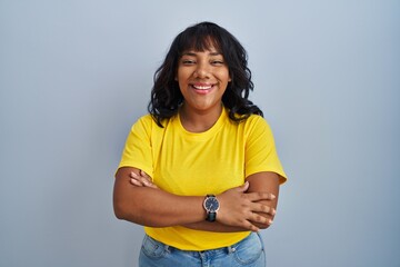 Hispanic woman standing over blue background happy face smiling with crossed arms looking at the camera. positive person.