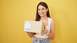 © Krakenimages.com - Young beautiful hispanic woman smiling confident holding package over isolated yellow background