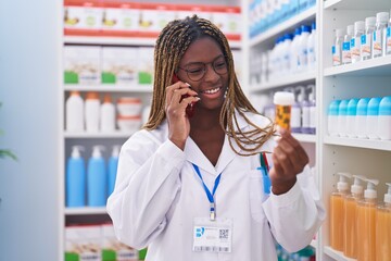 Poster - African american woman pharmacist holding pills bottle talking on smartphone at pharmacy