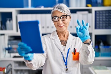 Poster - Middle age woman with grey hair working at scientist laboratory doing video call doing ok sign with fingers, smiling friendly gesturing excellent symbol