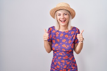 Poster - Young caucasian woman wearing flowers dress and summer hat success sign doing positive gesture with hand, thumbs up smiling and happy. cheerful expression and winner gesture.