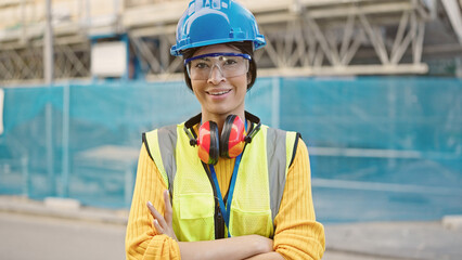 Wall Mural - Young beautiful hispanic woman architect smiling confident standing with arms crossed gesture at street