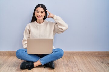 Wall Mural - Young woman using laptop sitting on the floor at home smiling pointing to head with one finger, great idea or thought, good memory