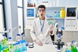 © Krakenimages.com - Young hispanic man working at scientist laboratory holding brazilian reals scared and amazed with open mouth for surprise, disbelief face