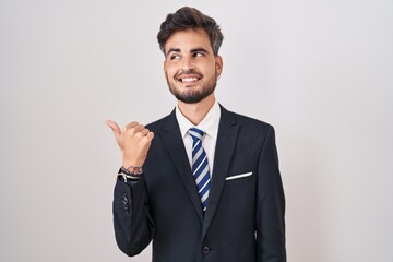 Poster - Young hispanic man with tattoos wearing business suit and tie smiling with happy face looking and pointing to the side with thumb up.