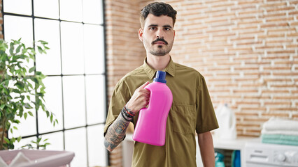 Sticker - Young hispanic man holding detergent bottle at laundry room