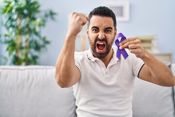 Canvas Print - Young hispanic man with beard holding purple ribbon awareness annoyed and frustrated shouting with anger, yelling crazy with anger and hand raised