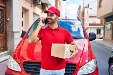 Sticker - Young hispanic man courier talking on the smartphone holding package at street