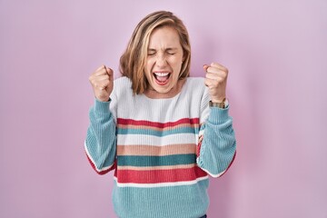 Canvas Print - Young blonde woman standing over pink background excited for success with arms raised and eyes closed celebrating victory smiling. winner concept.