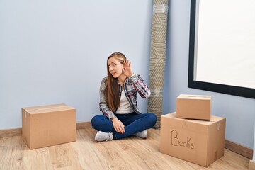 Sticker - Young blonde woman sitting on the floor moving to a new home smiling with hand over ear listening an hearing to rumor or gossip. deafness concept.