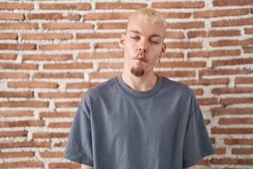 Sticker - Young caucasian man standing over bricks wall making fish face with lips, crazy and comical gesture. funny expression.