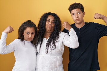 Poster - Family of mother, daughter and son standing over yellow background strong person showing arm muscle, confident and proud of power