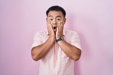 Poster - Chinese young man standing over pink background afraid and shocked, surprise and amazed expression with hands on face